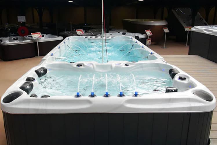 Vista di una grande vasca idromassaggio esposta in un negozio, con acqua che scorre e getti d'acqua attivi, circondata da altri modelli.