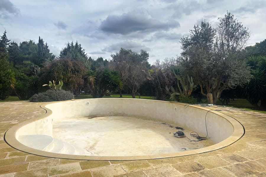 Piscina interrata in cemento armato svuotata e priva di rivestimento, pronta per lavori di ristrutturazione e ripristino.