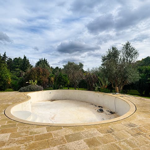 Piscina interrata in cemento armato svuotata e priva di rivestimento, pronta per lavori di ristrutturazione e ripristino.
